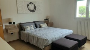 A bedroom with a bed, bedside tables, a bench, and a window with a view. - CASA MAFALDA Station area - historic center - theater with indoor parking. (Imola)