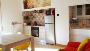 A compact kitchen with a refrigerator, stove, and microwave. There is a dining table with chairs and a red sofa. - CASA MAFALDA Station area - historic center - theater with indoor parking. (Imola)