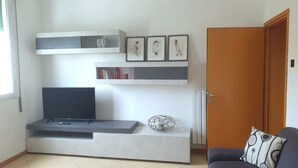 A living room with a flat-screen TV, a sofa, a coffee table, and a door. - CASA MAFALDA Station area - historic center - theater with indoor parking. (Imola)
