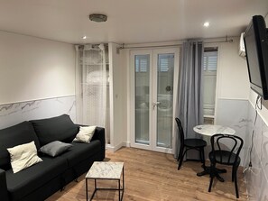 A modern living room with a black sofa, a small marble table, and a glass door leading to a balcony. - Charming studio in Nice,France (Nice)