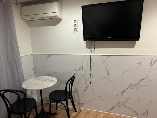 A small room with a TV mounted on the wall, a table with two chairs, and an air conditioning unit above the table. - Charming studio in Nice,France (Nice)