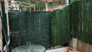 Un patio con una mesa redonda y sillas, un seto verde y suelo de baldosas.