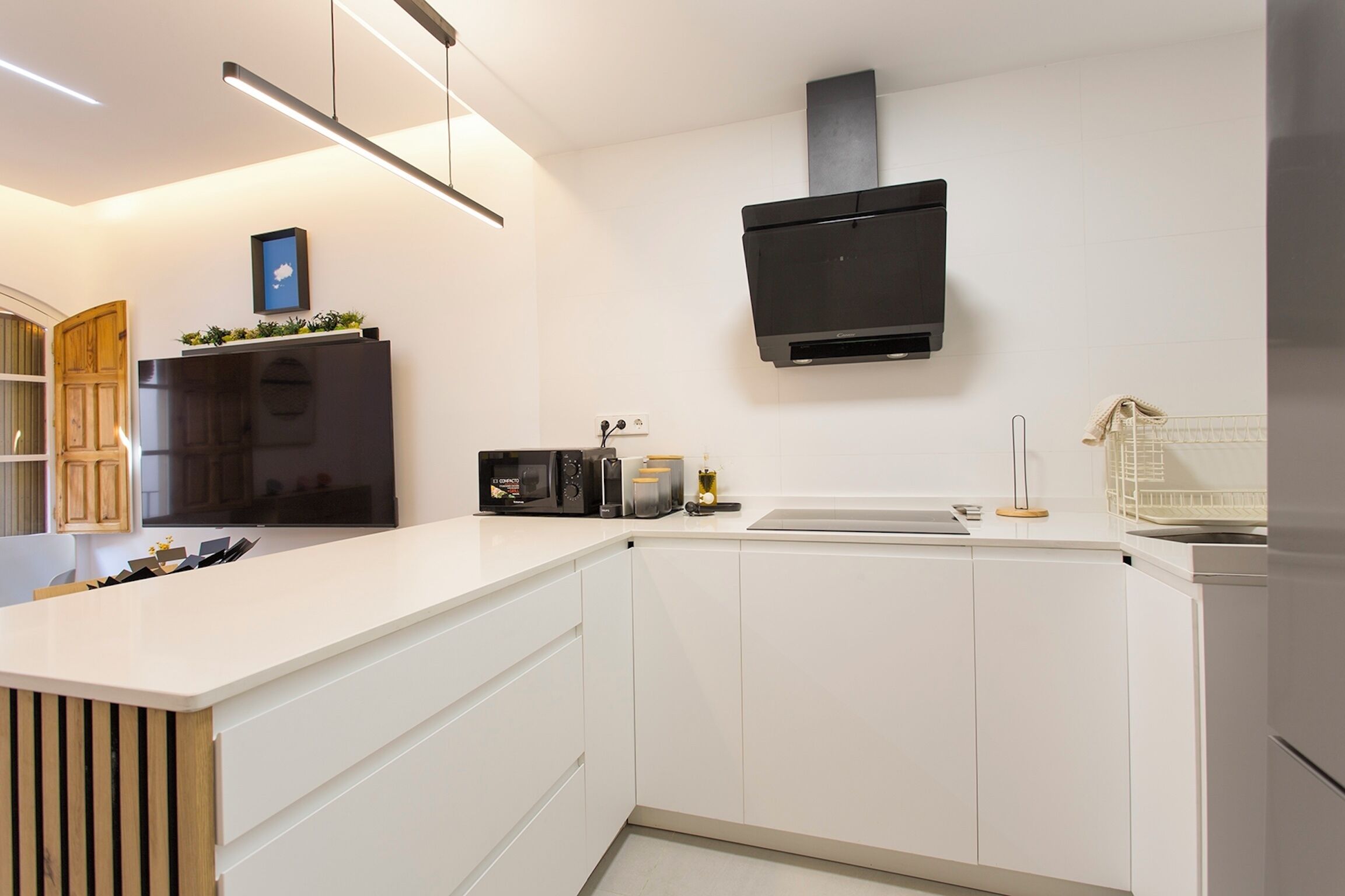 Una cocina moderna con armarios blancos, un microondas integrado y una campana extractora negra.