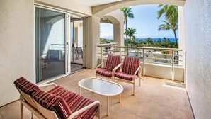 Ein Balkon mit Blick auf das Meer, zwei gestreifte Liegestühle, ein kleiner Tisch und eine Schiebetür.