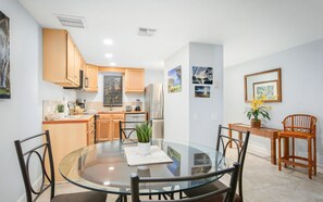 A modern kitchen with wooden cabinets, a refrigerator, and a dining area with a glass table and chairs.