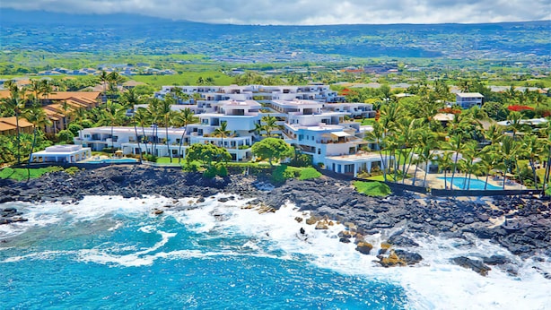A coastal resort with multiple white buildings, a rocky shoreline, and a view of the ocean and distant landscape. - Royal Sea Cliff Kona 202 Ocean View 1 Bedroom (Kailua Kona)