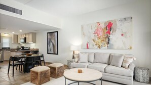 A modern living room with a sofa, ottomans, a coffee table, and a dining area with chairs and a table. - Royal Sea Cliff Kona 202 Ocean View 1 Bedroom (Kailua Kona)