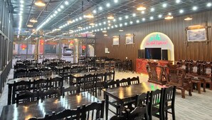 Un'ampia sala ristorante con numerosi tavoli e sedie, soffitto alto con travi a vista e insegna al neon per 'Van Anh Restaurant'.