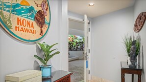 A hallway with a wooden table, a potted plant, a statue, and a wall with a 'Kona Hawaii' sign.