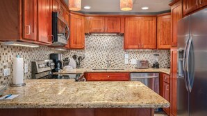 A kitchen with wooden cabinets, a granite countertop, stainless steel appliances, and a tiled backsplash.