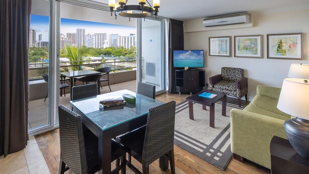 A modern hotel room with a balcony, a dining area, a TV, and artwork on the walls. - Regency on Beachwalk City View 1 Bedroom (Honolulu)