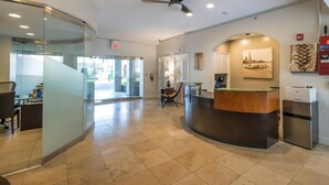 A reception area with a glass partition, a reception desk, a ceiling fan, and a view of the outside. - Regency on Beachwalk City View 1 Bedroom (Honolulu)
