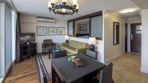 A hotel room with a dining table, chairs, a sofa, a TV, and artwork on the walls. - Regency on Beachwalk City View 1 Bedroom (Honolulu)