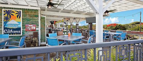 Un área de comedor al aire libre con mesas y sillas, un cartel que dice 'The Cabana Bar & Grill' y vistas del paisaje.