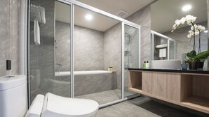 A modern bathroom with a glass-enclosed shower, a toilet with a control panel, a sink with a mirror, and a wooden vanity. - FLORAMOS HOTEL   (Tianzhong)