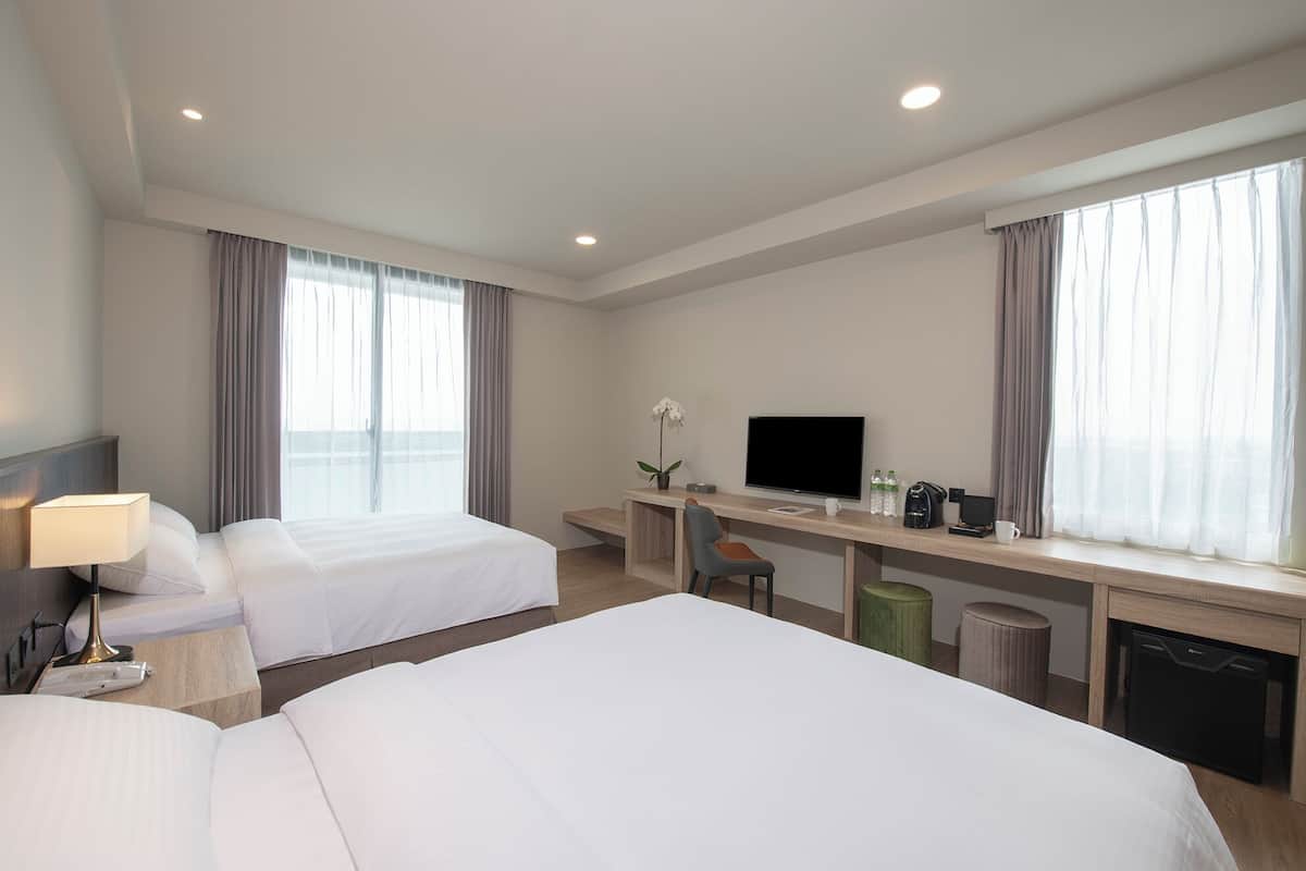 Quarto de hotel com duas camas, uma escrivaninha com televisão, cafeteira e uma planta.
