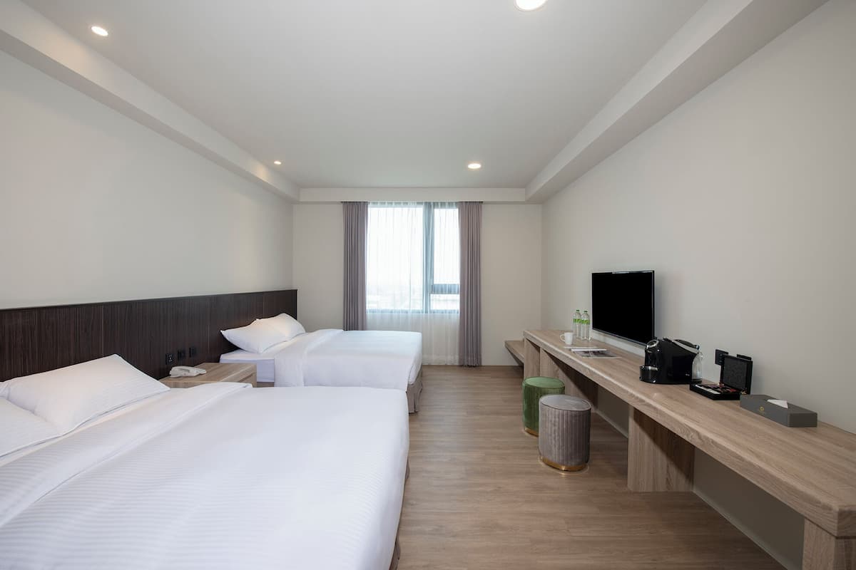 Quarto de hotel com duas camas, televisão, mesa com cafeteira e lixeira.