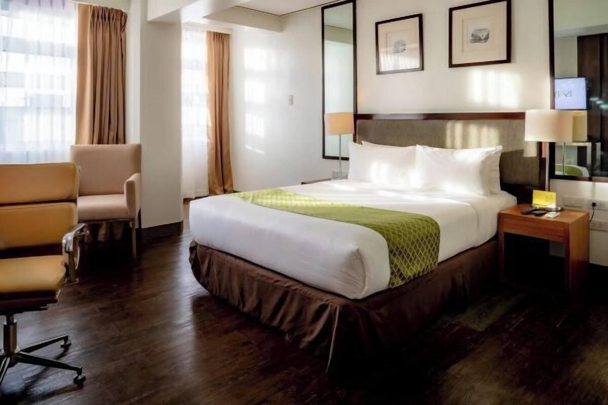 Une chambre d’hôtel avec un grand lit, un bureau, une chaise, une télévision et une fenêtre avec des rideaux.