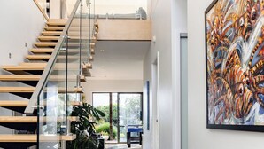 Un interior moderno con una escalera de cristal, un cuadro abstracto de gran tamaño y vistas al exterior.