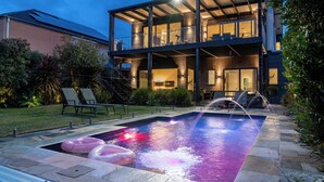 Una casa moderna de dos pisos con piscina, mobiliario exterior y un jardín bien cuidado.