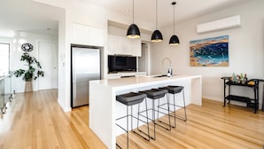Una cocina moderna con una isla central, taburetes de bar, iluminación colgante y un cuadro en la pared.