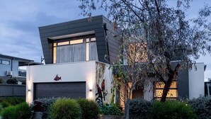 Una casa moderna de dos pisos con garaje, rodeada de jardines cuidados y un árbol.