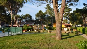 Leikkikenttä, jossa on monenlaisia leikkivälineitä, ja jonka ympärillä on puita ja nurmikkoalue.