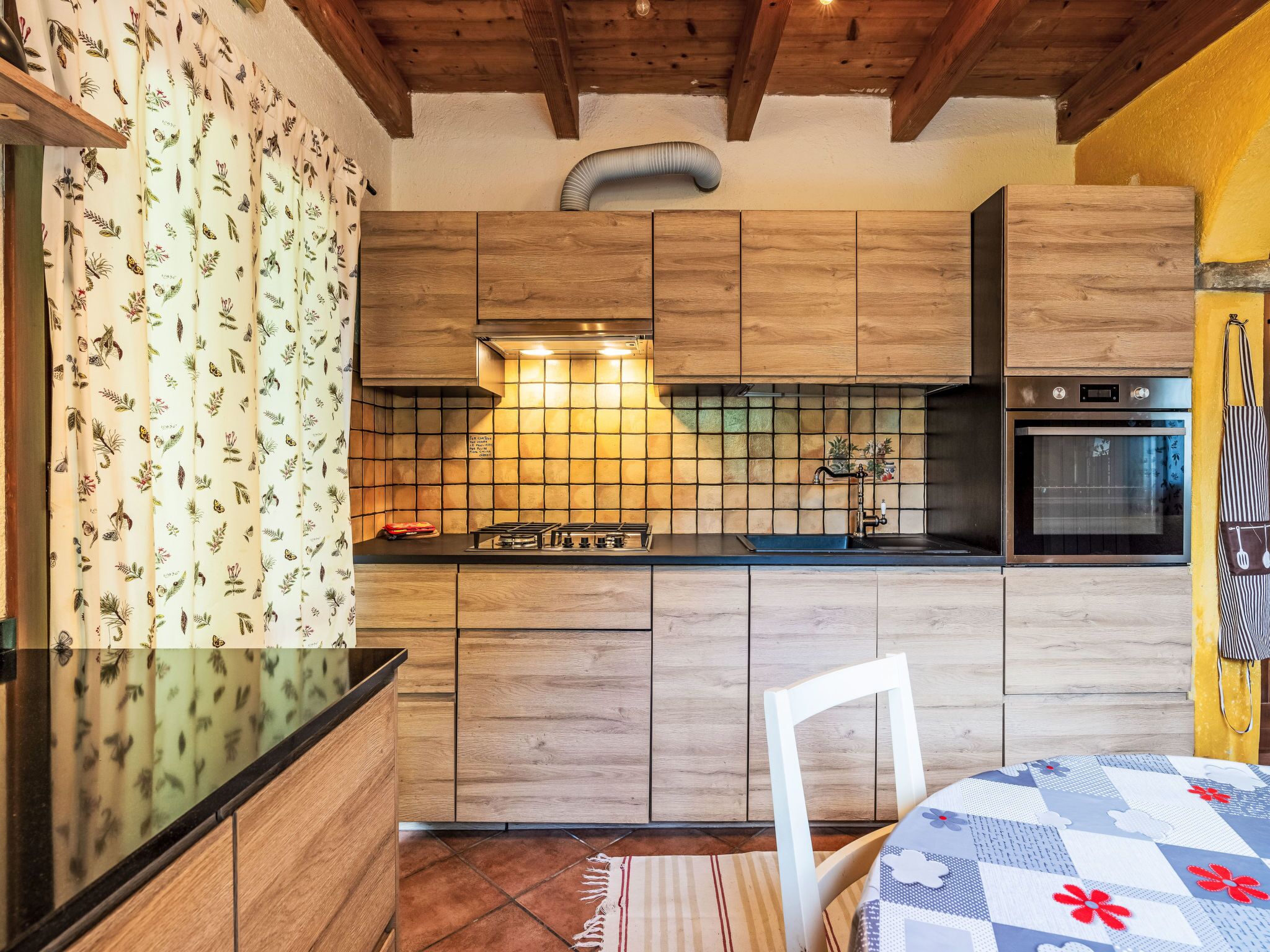 A kitchen with wooden cabinets, a gas stove, a built-in oven, and a window with a curtain.