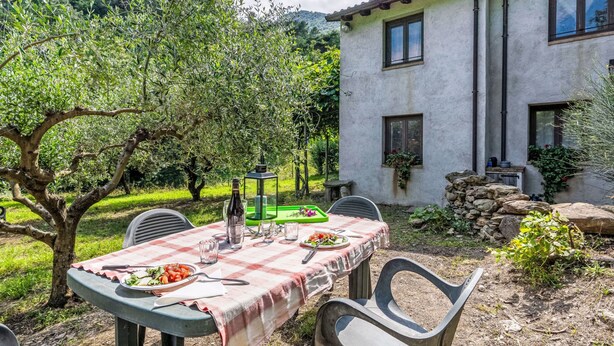 An outdoor dining area with a checkered tablecloth, a bottle of wine, and a plate of food. There are chairs around the table, and a building with stone walls and windows in the background. - La casa del Fiume by Interhome (Rialto)