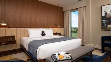 A hotel room with a large bed, a bedside table with a lamp, a view of the outdoors, and a breakfast tray on the bed.