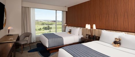 Habitación de hotel con dos camas, un escritorio, una silla y un ventanal con vistas al exterior.