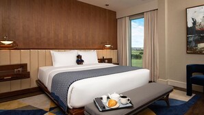 A hotel room with a large bed, a bedside table with a lamp, a view of the outdoors, and a breakfast tray on the bed.