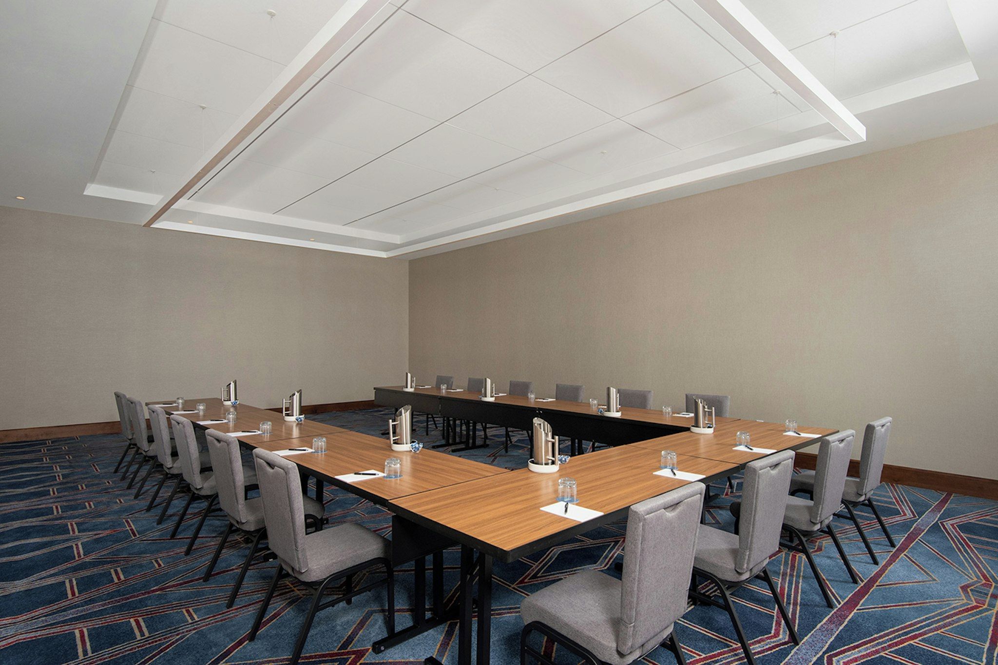 Sala de conferências com uma mesa comprida, cadeiras e piso coberto por carpete.