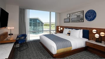 A hotel room with a large bed, a desk with a chair, a TV, and a view of a building through the window.