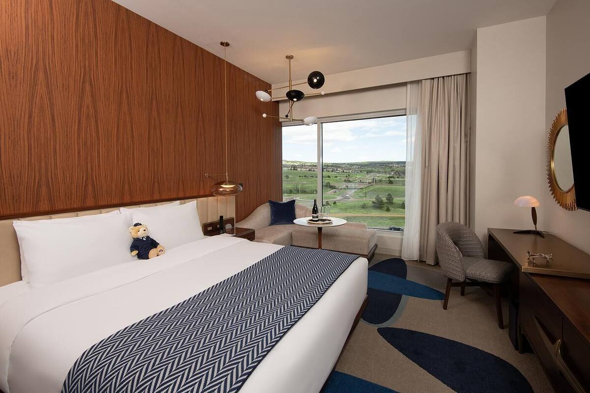 Habitación de hotel con una cama grande, un sofá, un escritorio y una silla. Se ve una ventana con vistas al campo.