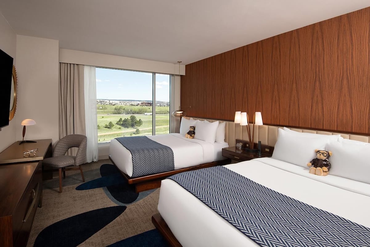 Habitación de hotel con dos camas, un escritorio, una silla y un ventanal con vistas al exterior.