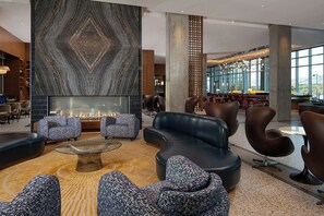 A modern lobby with a central fireplace, leather seating, and a view of the dining area. - Hotel Polaris (Colorado Springs)