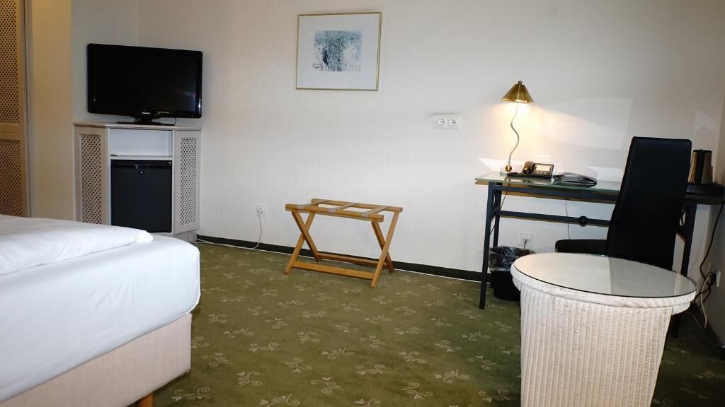 Une chambre d’hôtel comprenant un lit, un bureau avec une lampe, une télévision et une petite table.