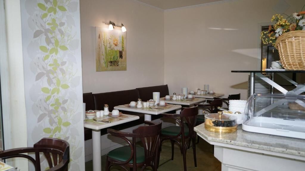 Un restaurante con mesas dispuestas para comer, sillas, una barra con vitrina y una pared con un cuadro de flores.