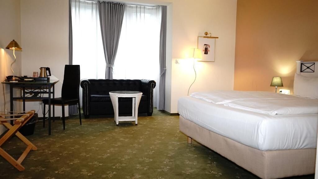 A hotel room with a bed, a desk, a chair, a small table, and a sofa.