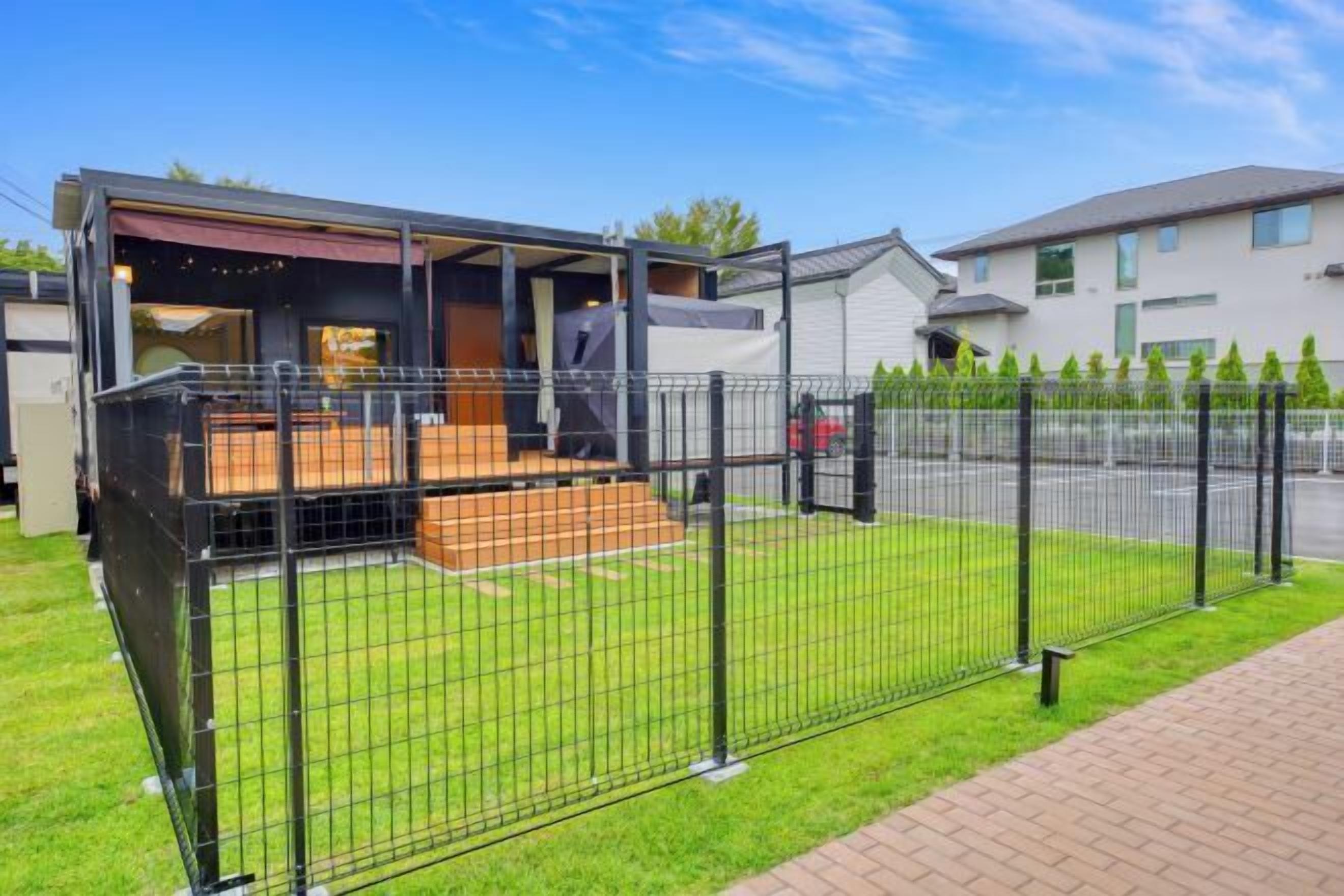 Una casa moderna con patio trasero cercado, zona de estar exterior cubierta y entrada pavimentada.