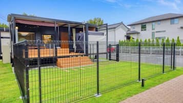 A modern house with a fenced backyard, a covered outdoor seating area, and a paved driveway.