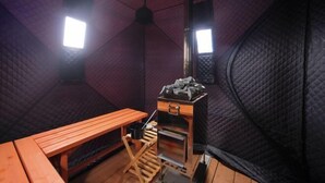 A cozy, insulated room with a wooden bench, a small table, and a wood-burning stove. - Piilo asobi＆stay (Yamanakako)