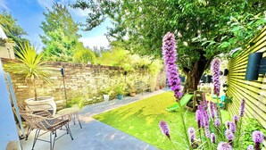 Un jardin avec un espace patio, un mur en briques et une variété de plantes et de fleurs.