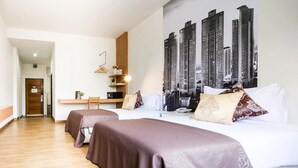 A hotel room with two beds, a desk, and a large cityscape mural on the wall.