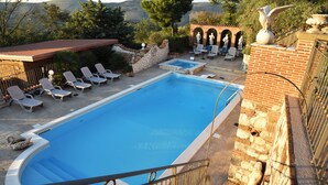 A rectangular swimming pool with a stone border, surrounded by lounge chairs and a small seating area with a table.