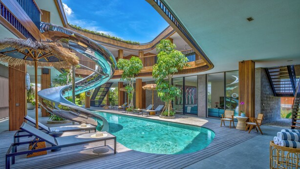 Un espace piscine intérieur moderne doté d’un toboggan en spirale, de chaises longues et d’une terrasse en bois.