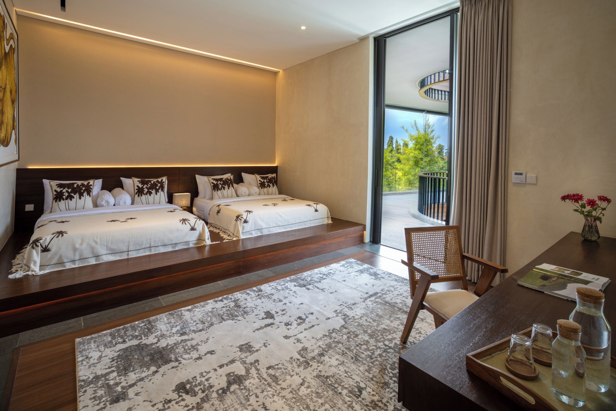 Una habitación de hotel moderna con dos camas, un ventanal grande, un balcón y un escritorio de madera con una bandeja de botellas.