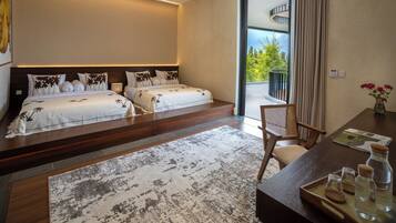 Una habitación de hotel moderna con dos camas, un ventanal grande, un balcón y un escritorio de madera con una bandeja de botellas.