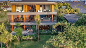 Une maison moderne à deux étages, dotée d’un balcon, d’un espace salon extérieur et d’une végétation luxuriante.